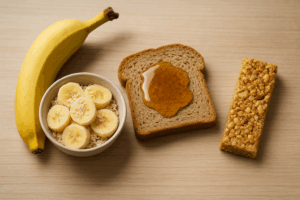 Tigela com aveia e banana, fatia de pão integral com mel e barra de cereal sobre uma superfície de madeira clara.