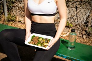 Alimentação pré treino: mulher com top branco, calça preta  alimentos.